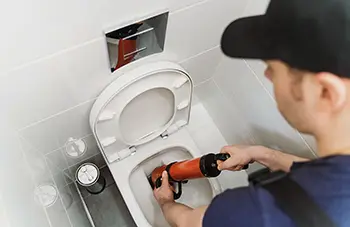 Plumber unclogging toilet with professional force pump cleaner.