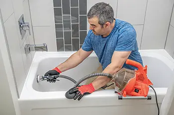 Man using a mini plumbers snake to unclog a bathtub drain